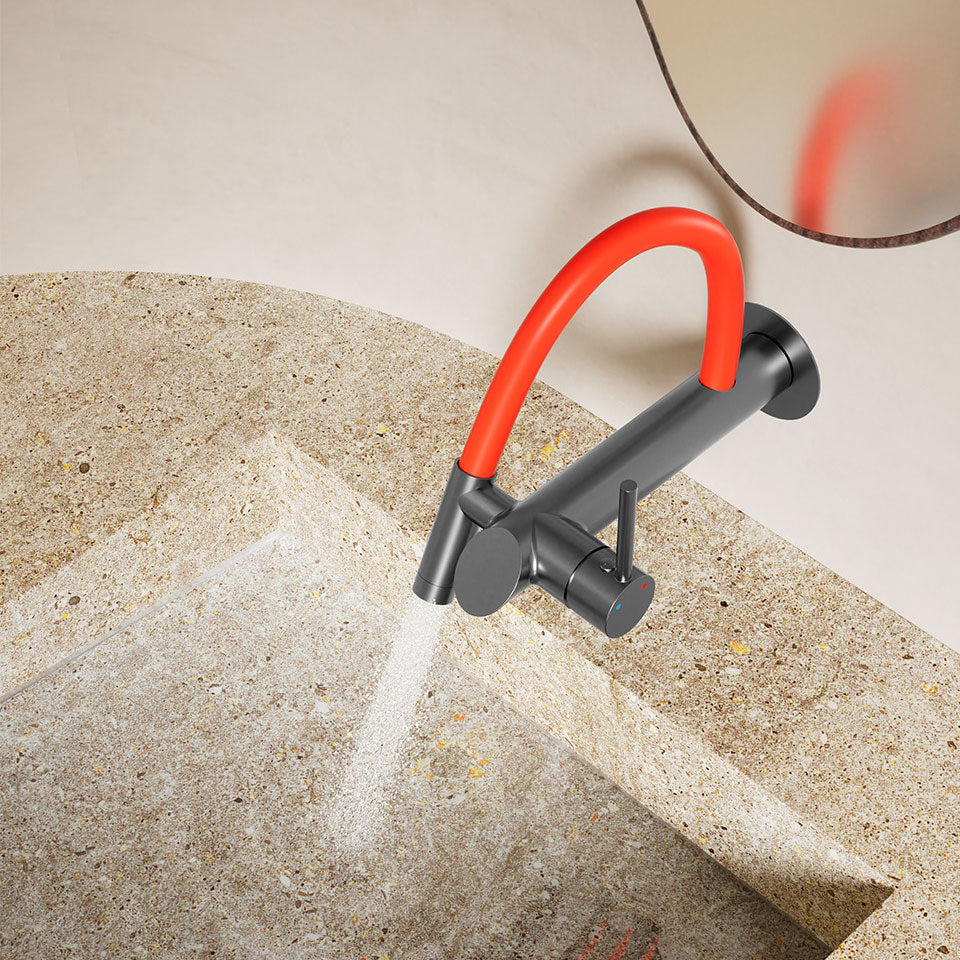 A top-down perspective view of a sleek wall-mounted bathroom faucet in brushed gunmetal grey with a vibrant red flexible neck, delivering a soft aerated water stream into a modern beige terrazzo vanity basin