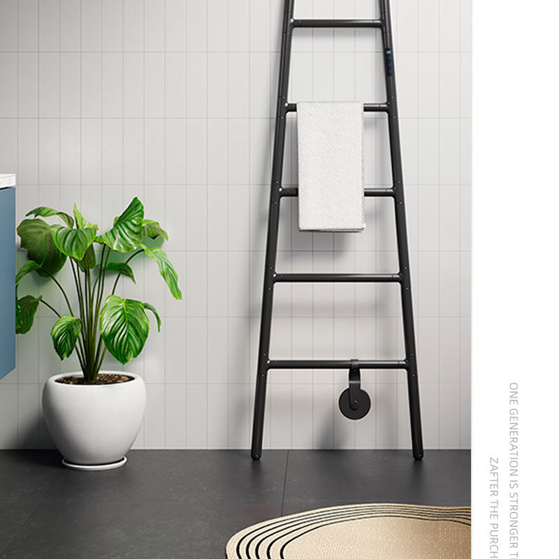 Sleek matte black ladder-style electric heated towel warmer with a smart touch interface, leaning against a white vertical tiled wall in a modern bathroom setup next to a green potted plant.