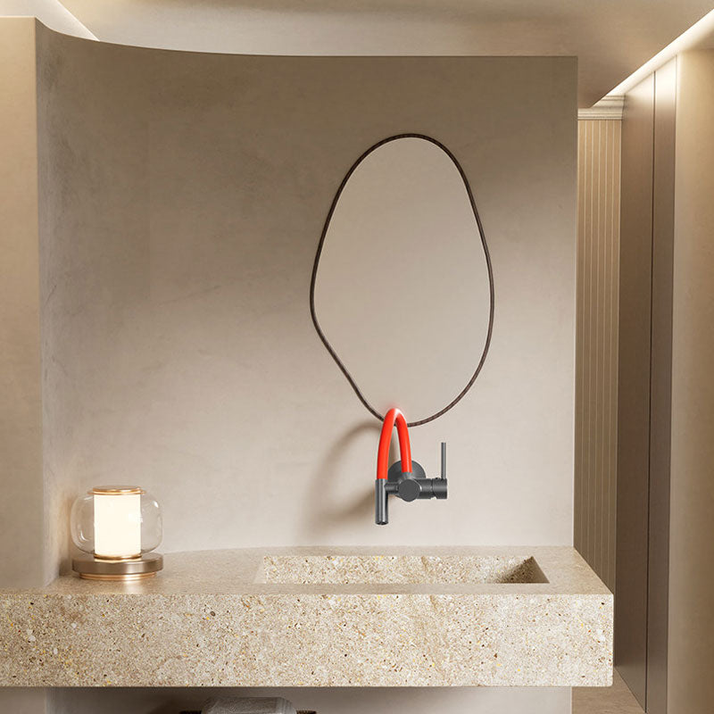 Modern bathroom interior design in earthy microcement finish, featuring an irregular shape mirror, a beige terrazzo sink vanity, and a wall-mounted gunmetal grey faucet with a vibrant red silicone spout.